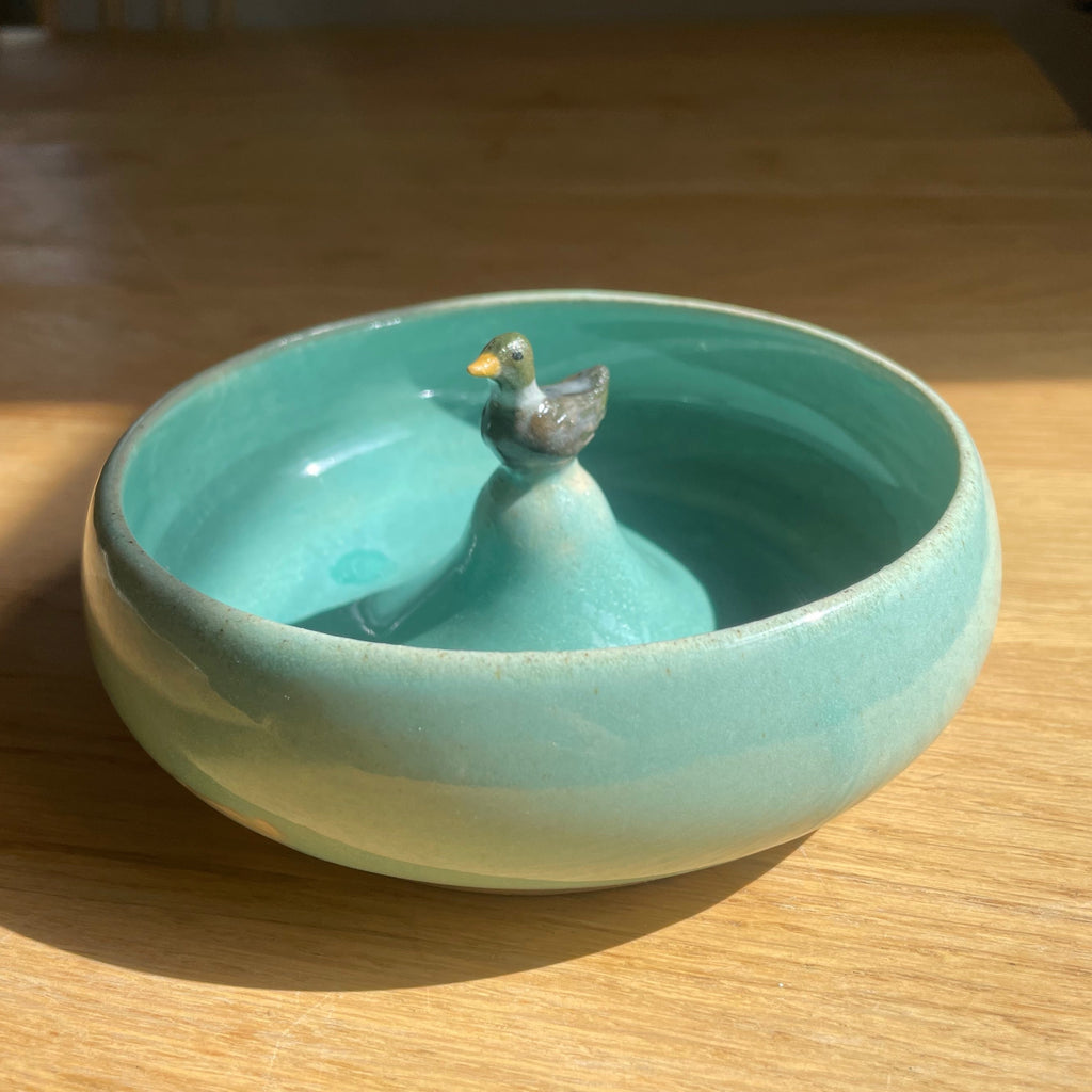 Turquoise ceramic bowl with a small bird figurine