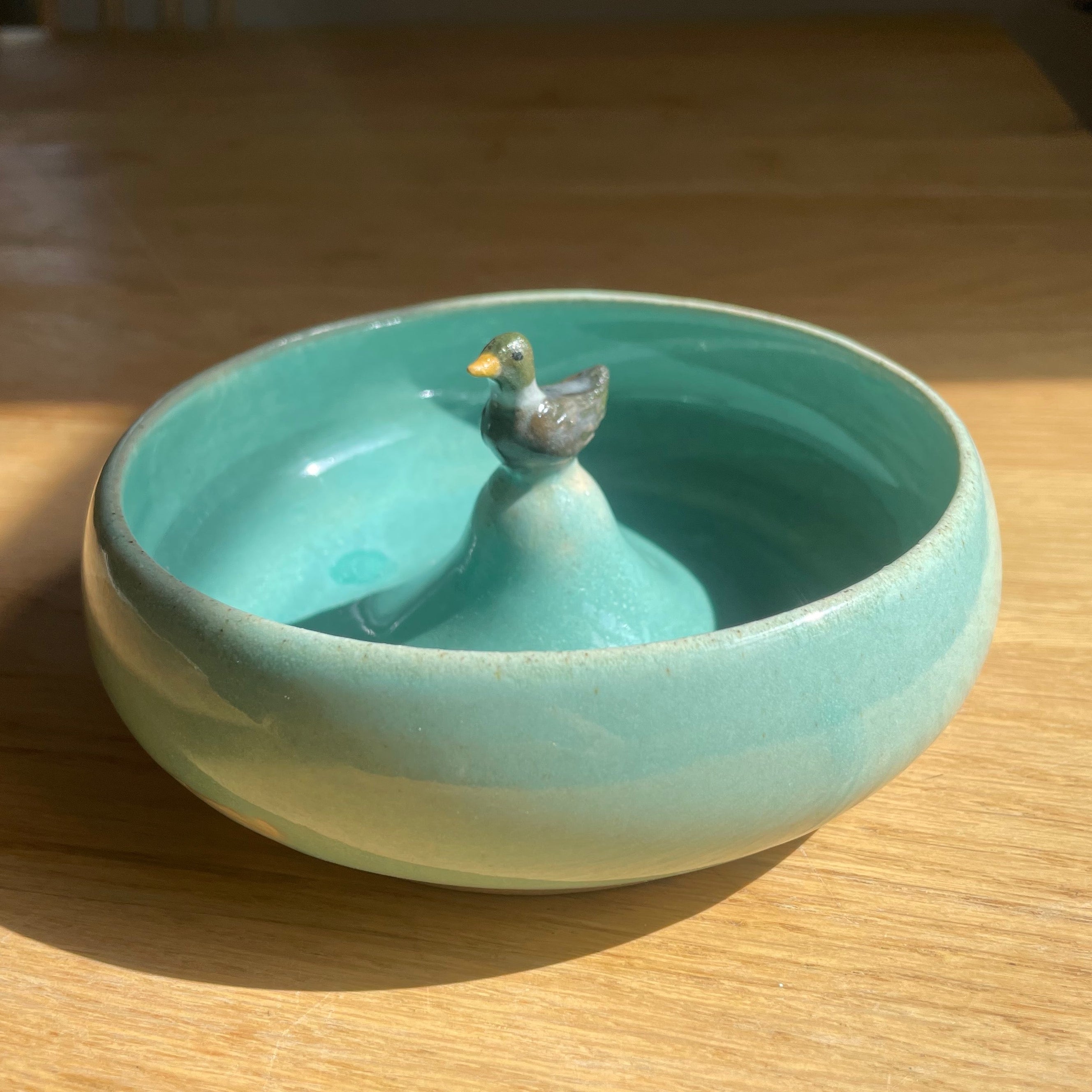 Turquoise ceramic bowl with a small bird figurine